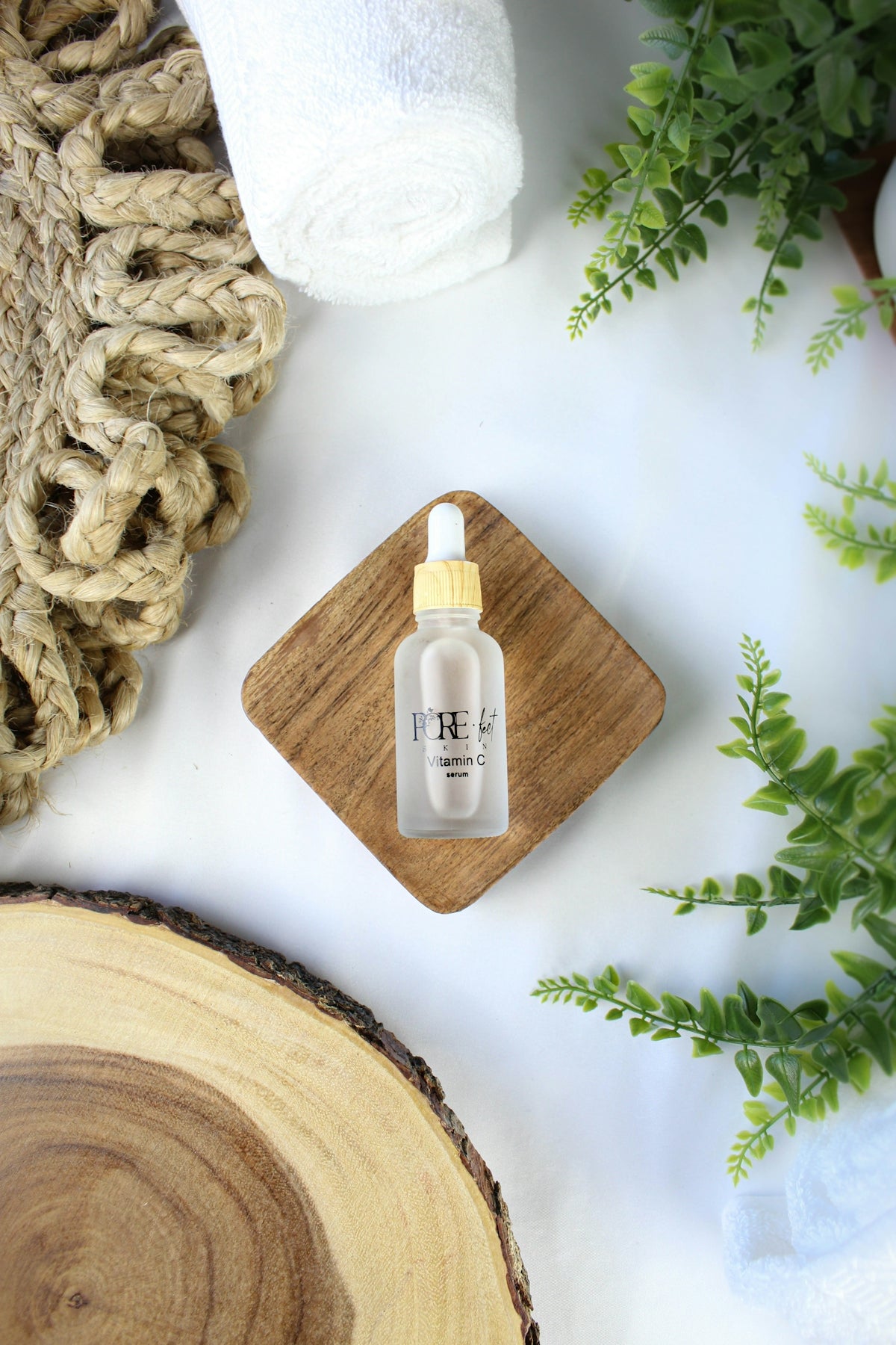 A small bottle of serum with greenery and towels.